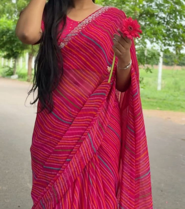 Woman in a red saree standing outdoors with greenery in the background